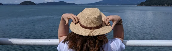 Sabrina Busch mit Sonnenhut, blickt aufs Meer von einem Geländer aus im Urlaub.