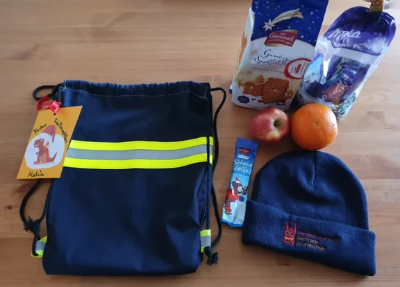 Neben einem Turnbeutel liegen Süßigkeiten, Obst und eine Mütze.