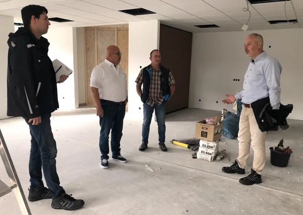 Eine Personengruppe in einem Raum, der offensichtlich eine Baustelle ist.
