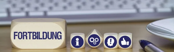 Ein großer und vier kleine Würfel nebeneinander in Nahaufnahme. Auf dem großen Würfel steht das Wort "Fortbildung", die kleinen zeigen jeweils ein weißes Symbol in einem blauen Kreis: der Kleinbuchstabe i, drei Zahnräder, eine Kopfsilhouette mit einem Ausrufezeichen und einen "Daumen hoch".