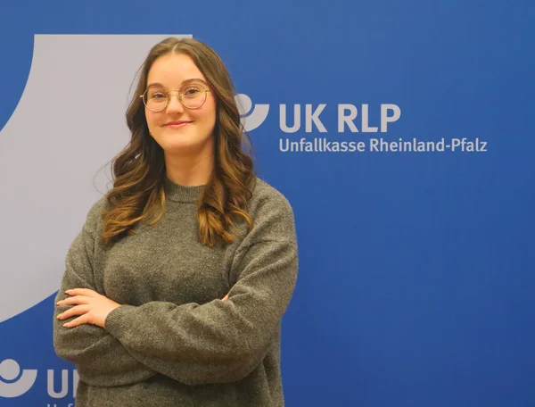 Die Auszubildende Marie Schmidt steht vor der Pressewand der Unfallkasse.