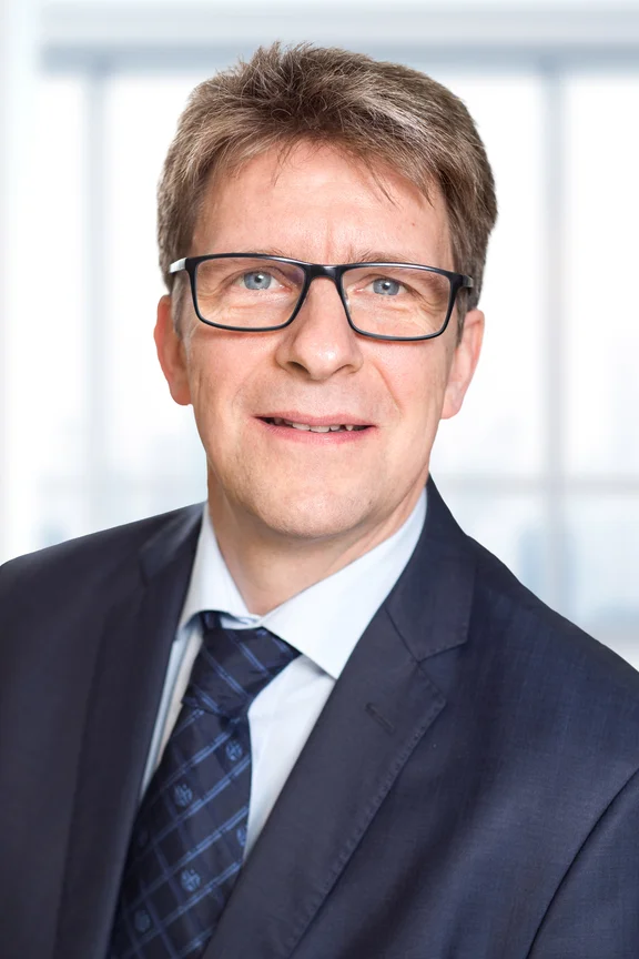 Portrait von Dr. Christoph Heidrich: Er trägt Anzug, eine Brille und hat blonde Haare. 