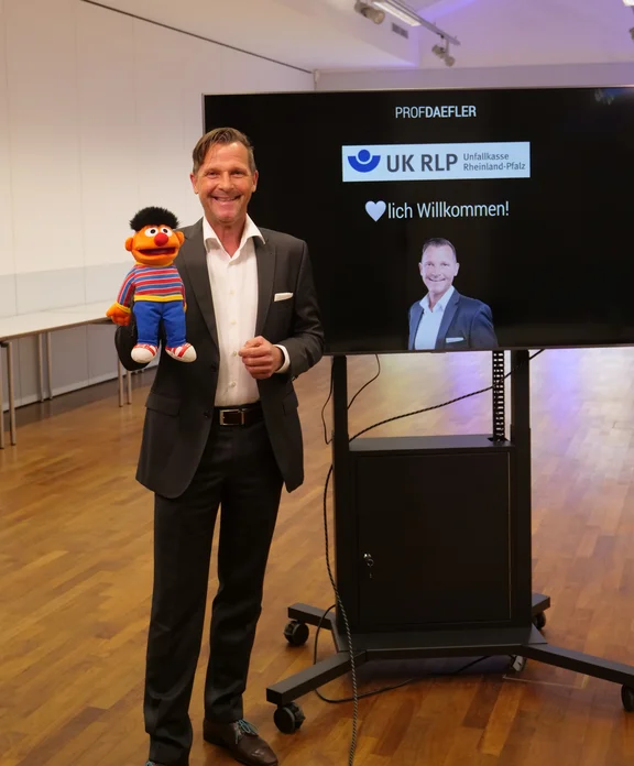 Ein Mann steht mit einer Handpuppe von einem Fernseher.