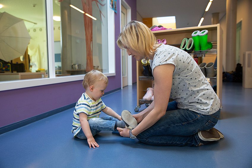 Eine Erzieherin hilft einem Kind beim Anziehen der Schuhe.