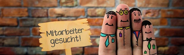 Vier Finger einer Hand sind jeweils mit einem freundlichen Gesicht bemalt. Neben den Fingern ist ein Schild abgebildet, auf dem steht: Mitarbeiter gesucht!