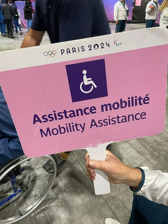 Eine Hand hält ein Schild mit der Aufschrift "Assistance mobilité – Mobility Assistance".