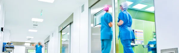 Ein Krankenhausflur vor den Operationssälen. Darin steht Krankenhauspersonal mit OP-Häubchen und Mundschutz. 