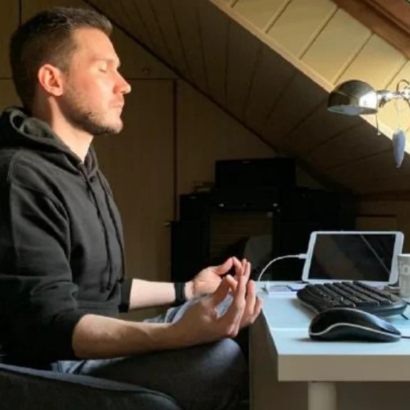ein junger Mann in Meditationshaltung an seinem Schreibtisch