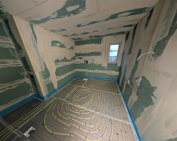 Blick in das umgeplante Bad, noch mit rohen Wänden und freiliegenden Leitungen der Fußbodenheizung.