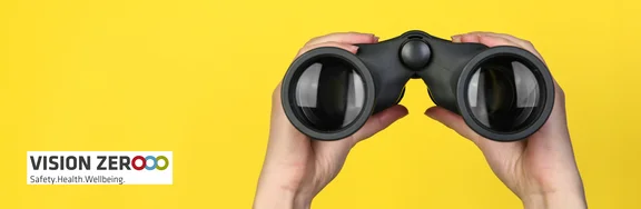 Vor einem gelben Hintergrund halten zwei Hände ein Fernglas links und rechts fest. Das Fernglas ist auf den Betrachter gerichtet. Daneben das Logo der Vision Zero.