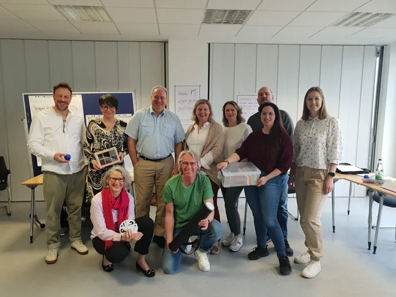 Eine Gruppe von Menschen steht vor Tischen und Flipcharts.