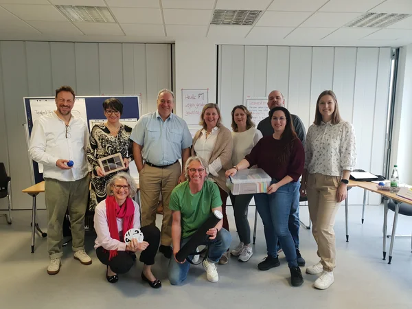 Eine Gruppe von Menschen steht vor Tischen und Flipcharts.