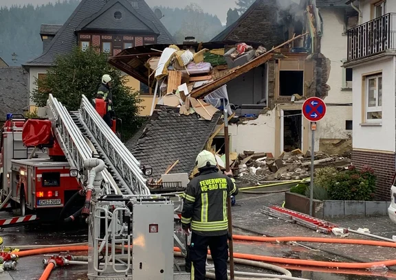 Vor einem eingestürzten Haus steht ein Feuerwehrmann neben einem Feuerwehrwagen.