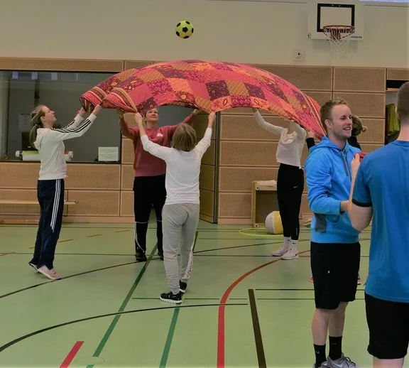 Vier Frauen halten je einen Zipfel einer aufgespannten Decke und katapultieren damit einen Ball in die Luft.