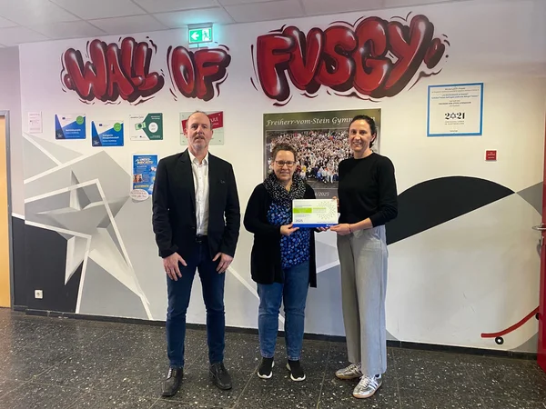 Eine Personengruppe mit einem Mann und zwei Frauen. Die beiden Frauen halten die Präventionspreis-Plakette.