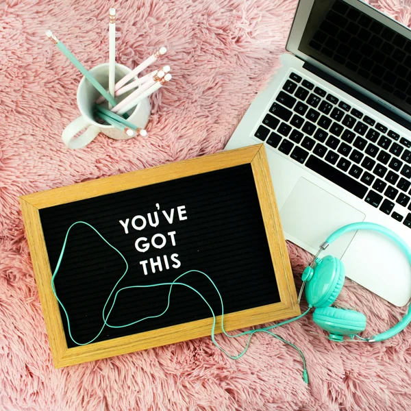 Laptop, Kopfhörer, eine Tasse mit Stiften und eine Tafel mit der Aufschrift "You've got this!"