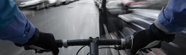 Straßenansicht aus der Sicht eines oder einer Radfahrenden. Zu sehen sind Lenker und Hände des oder der Fahrenden. Und eine Autotür, die sich wenige Meter voraus plötzlich öffnet.