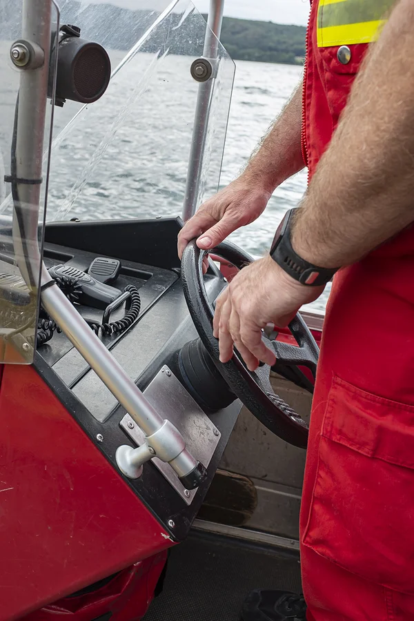 Die Arme einer im Boot stehenden DLRG-Rettungskraft. Die Hände lenken das Boot.