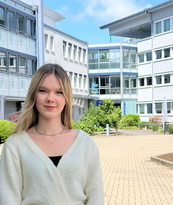 Junge blonde Frau steht vor einem weißem Bürogebäude. (Unfallkasse Rheinland-Pfalz)