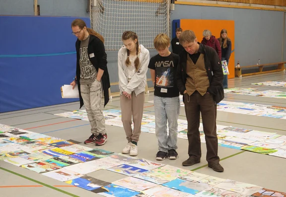 Zwei Jugendliche und zwei Erwachsene schauen sich Bilder an, die vor ihnen auf dem Boden liegen. 