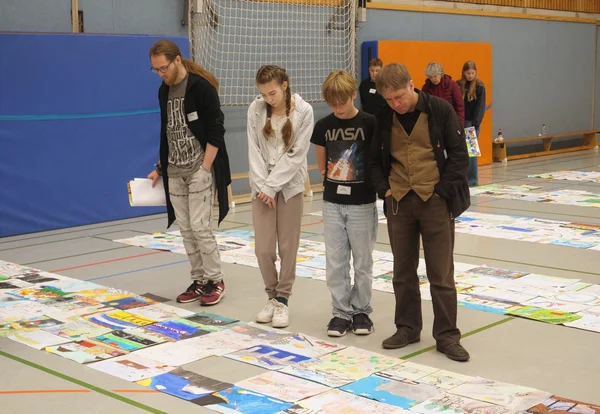 Zwei Jugendliche und zwei Erwachsene schauen sich Bilder an, die vor ihnen auf dem Boden liegen. 