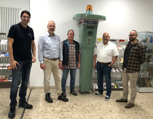 Eine Personengruppe, gruppiert um eine alte Notrufsäule.