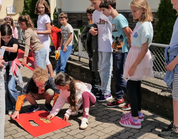 Kinder stehen auf dem Gehweg. Einige von ihnen hocken am Boden, um mit Pinsel und Schablone gelbe Füße aufzumalen. 