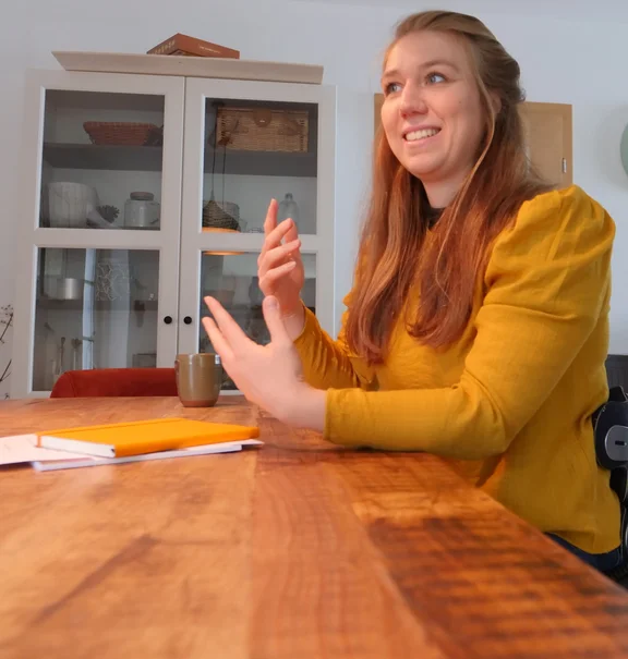 Sabrina Busch sitzt am Tisch im Gespräch und gestikuliert lächelnd mit den Händen.