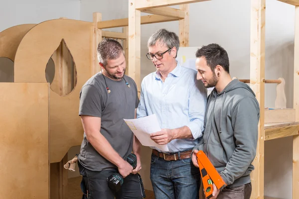 Drei Männer besprechen sich auf einer Baustelle und zeigen auf einen Plan