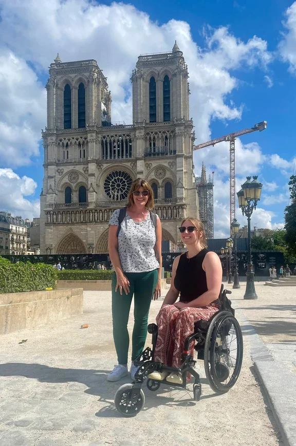 Zwei Frauen, eine davon im Rollstuhl, posieren für ein Foto vor der Kirche Notre Dame.