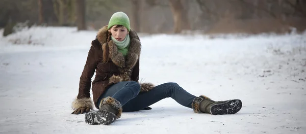 Eine Frau sitzt erschrocken auf schneeglattem Boden, nachdem sie gestürrzt ist.
