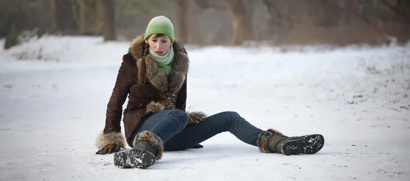 Eine Frau sitzt erschrocken auf schneeglattem Boden, nachdem sie gestürrzt ist.