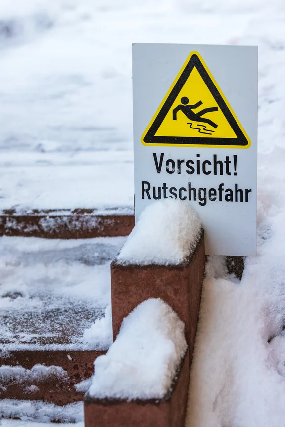 Schneebedecktes Gelände und ein Schild mit der Aufschrift "Vorsicht! Rutschgefahr".