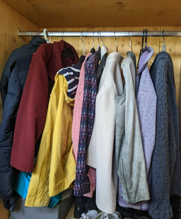 Blick in den Kleiderschrank: mehrere Kleidungsstücke hängen auf Kleiderbügeln an einer Kleiderstange
