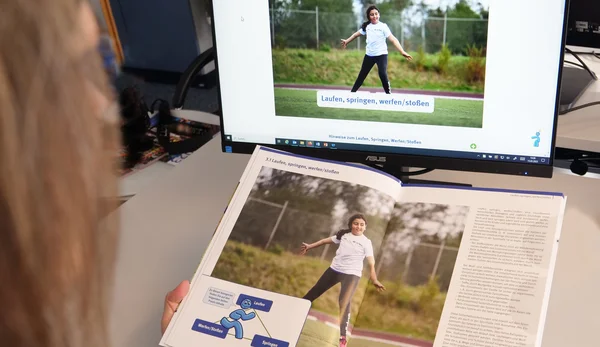 Eine Frau schaut in das Buch Schulsportideen und in die Website schulsportideen.de.