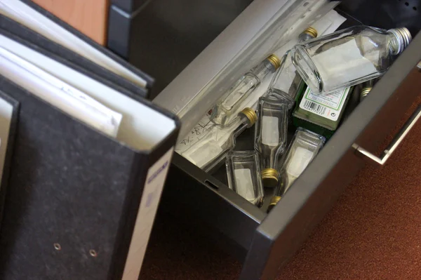 Blick in eine geöffnete Büroschrank-Schublade, in der viele leere Schnapsfläschchen liegen. 